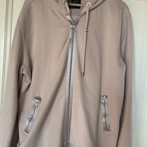 Beige hoodie Limitato x Bardot - Säljer en beige hoodie med inslag av rosa  från Limitato med Brigitte Bardot-tryck på ryggen. Tröjan har huva, dragkedja framtill och två fickor med silvriga dragkedjor. Snygga detaljer och coolt fotoprint gör den unik. Perfekt för dig som gillar streetstyle. ⚠️Box finns ⚠️