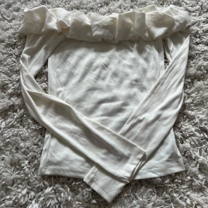 Vit söt offshoulder volangtop från Amisu - Supersöt vit offshoulder topp från Amisu med bred volang längs hela överkanten. Långärmad och figurnära passform, perfekt för dig som gillar en stilren men ändå lekfull look. Mjuk och stretchig i bomullsmix.