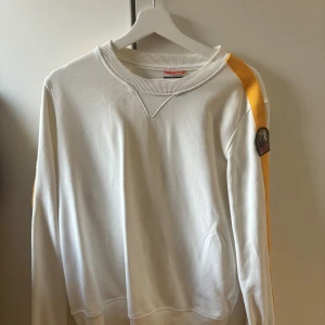 Vit fleecetröja Parajumpers - Säljer en vit fleece-tröja från Parajumpers i storlek M. Tröjan har en gul rand längs ena ärmen och ett snyggt P.J.S märke på axeln.
