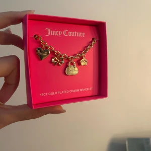 Juicy Couture guldpläterat armband - NYTT! Charmigt armband från Juicy Couture i 18 karats guldplätering. Armbandet har flera hängen, bland annat ett hjärta, en rosett, en väska och en krona. Kommer i en snygg rosa ask med logga. Perfekt accessoar för dig som gillar statement-smycken. Nypris ca 200 dollar