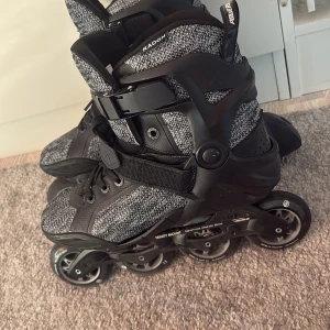 Svarta och grå Powerslide inlines - Säljer ett par Powerslide Phuzion Radon inlines i svart och grått med stickad textil och robust plast. De har snörning, kardborreband och spänne för extra stöd. Perfekta för dig som vill cruisa runt i stan eller träna på cykelvägarna.