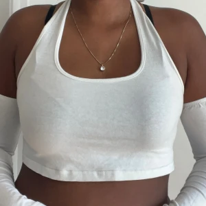 Vit croppad halterneck linnetopp - Snygg vit croppad halterneck linnetopp med ärmlösa avtagbara ärmar. Perfekt för sommardagar och enkel att matcha med jeans eller kjol. Toppens material är mjuk bomull och den har en stilren, minimalistisk look.