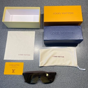 Bruna Louis Vuitton solglasögon - Säljer ett par snygga Louis Vuitton solglasögon med bred brun båge och stora bruna glas. Glasen har LV-monogram som mönster och modellen är LV1082. Kommer med originalfodral, putsduk och box. Perfekt för dig som vill sticka ut med lyxig design.