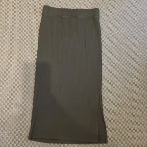 Olivgrön ribbad långkjol från 157 - Säljer en olivgrön långkjol från 157 i storlek S. Kjolen är ribbad med en rak passform och har en liten slits på sidan. Materialet är mjukt och stretchigt, perfekt för en chill och stilren look.