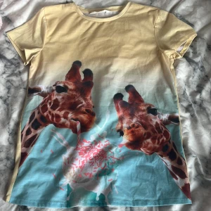 Gul t-shirt med girafftryck - Unik t-shirt i bomull med coolt tryck av två giraffer som dricker milkshake med strössel. Färgen går från ljusgul upptill till ljusblå nedtill, med korta ärmar och rund hals. Perfekt för dig som gillar djurmotiv och färgglada plagg. Knappt använd!