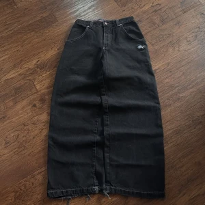 Svart lång jeanskjol från JNCO Jeans - Cool svart lång jeanskjol från JNCO Jeans med rå kant nertill och stora fickor bak. Snygg broderad detalj på ena bakfickan och klassiska kontrastsömmar. Perfekt för dig som gillar streetstyle och vill sticka ut lite extra.