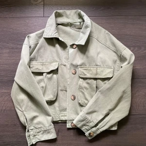 Grön croppad jeansjacka från Gina Tricot - Snygg jeansjacka från Gina Tricot med stora fickor framtill och knappar i trälook