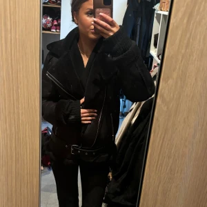 Svart vadderad skinnjacka  från Pieces - Säljer en svart skinnjacka från Pieces med bred krage, synliga dragkedjor och bälte i midjan. Jackan har långärmade ärmar och mjukt fuskpälsfoder som syns vid krage och muddar. Perfekt för dig som gillar en cool och chunky look.