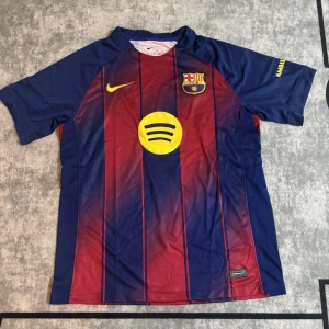 FC Barcelona fotbolls tröja - Säljer en officiell FC Barcelona matchtröja från Nike i storlek M. Tröjan har klassiska blå och röda vertikala ränder, klubbmärke på bröstet, gul Nike-logga och sponsortryck från Spotify. Tillverkad i lätt och ventilerande Dri-FIT-material.