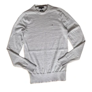 Ljusgrå ulltröja Tommy Hilfiger XS - Snygg ljusgrå stickad tröja från Tommy Hilfiger i lyxig ull. Klassisk rund halsringning och diskret logga broderad på bröstet. Perfekt för dig som gillar stilrena och tidlösa plagg med premiumkänsla.