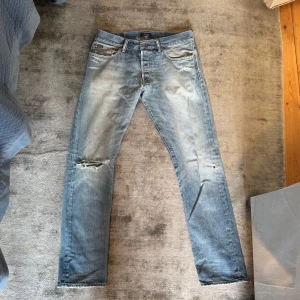 Ljusblå slitna jeans  - Ljusblå jeans från rahlp lauren med slitningar och hål på vänster knä och mindre hål på höger ben. Klassisk femficksmodell med raka ben och låg midja. Jeansen har en snygg tvättad look och är gjorda i jeansmaterial. 32/32 