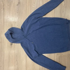 Blå hoodie - Säljer en snygg blå hoodie med långa ärmar och en praktisk huva. Perfekt för kyliga dagar och avslappnade stunder. Den har en enkel design utan mönster och är gjord i ett mjukt material.