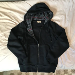 Svart hoodie från Burberry - Jätte snygg kofta från burberry som inte kommer till någon användning. Koftan har klassiskt rutig design på insidan längst dragkedjan och riktigt tung material som garanterar att den håller länge. Storlek M men passar som L, Nästan helt ny med tags och alltig. 🔸Kom gärna med prisförslag 🔸