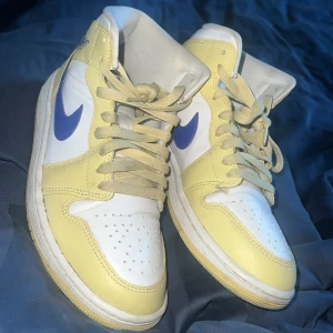 Nike Air Jordans i gult och vitt - Snygga Nike Air Jordans i en fräsch kombination av gult och vitt med blå detaljer. Skorna har en klassisk hög design med snörning och rund tå. Perfekta för dig som vill ha en stilren och sportig look.