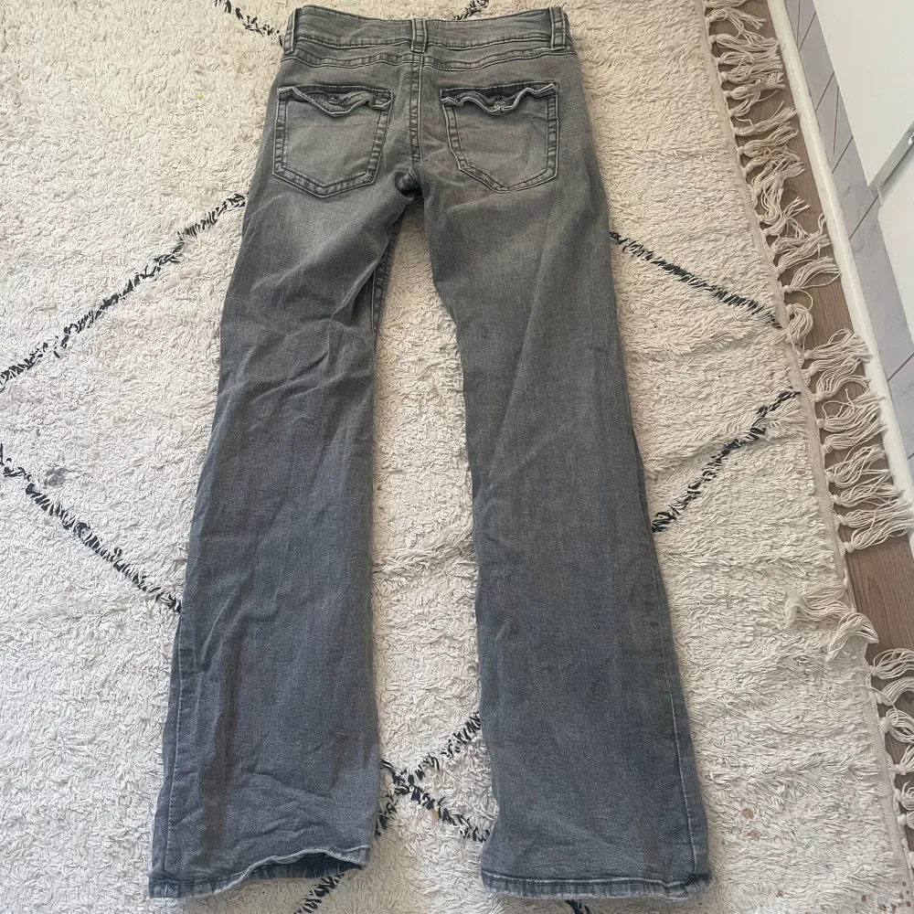 Snygga grå bootcut jeans med låg midja och klassisk femficksdesign. Jeansen har en dragkedja och knapp framtill. Perfekta för en avslappnad stil.. Farkut & Housut.