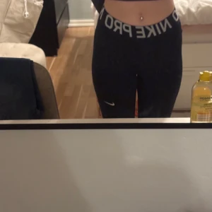 Svarta träningstights från Nike - Säljer ett par svarta träningstights från Nike med Dri-FIT-teknologi. Tightsen har en mellan hög midja och en liten Nike-logga på benet. Perfekta för träning och ger en bekväm passform.