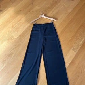 Svarta vida byxor från ONLY - Snygga svarta byxor från ONLY med hög midja och vida ben. Perfekta för en stilren look. Tillverkade i ett lätt och luftigt material som ger en skön känsla. Fickor