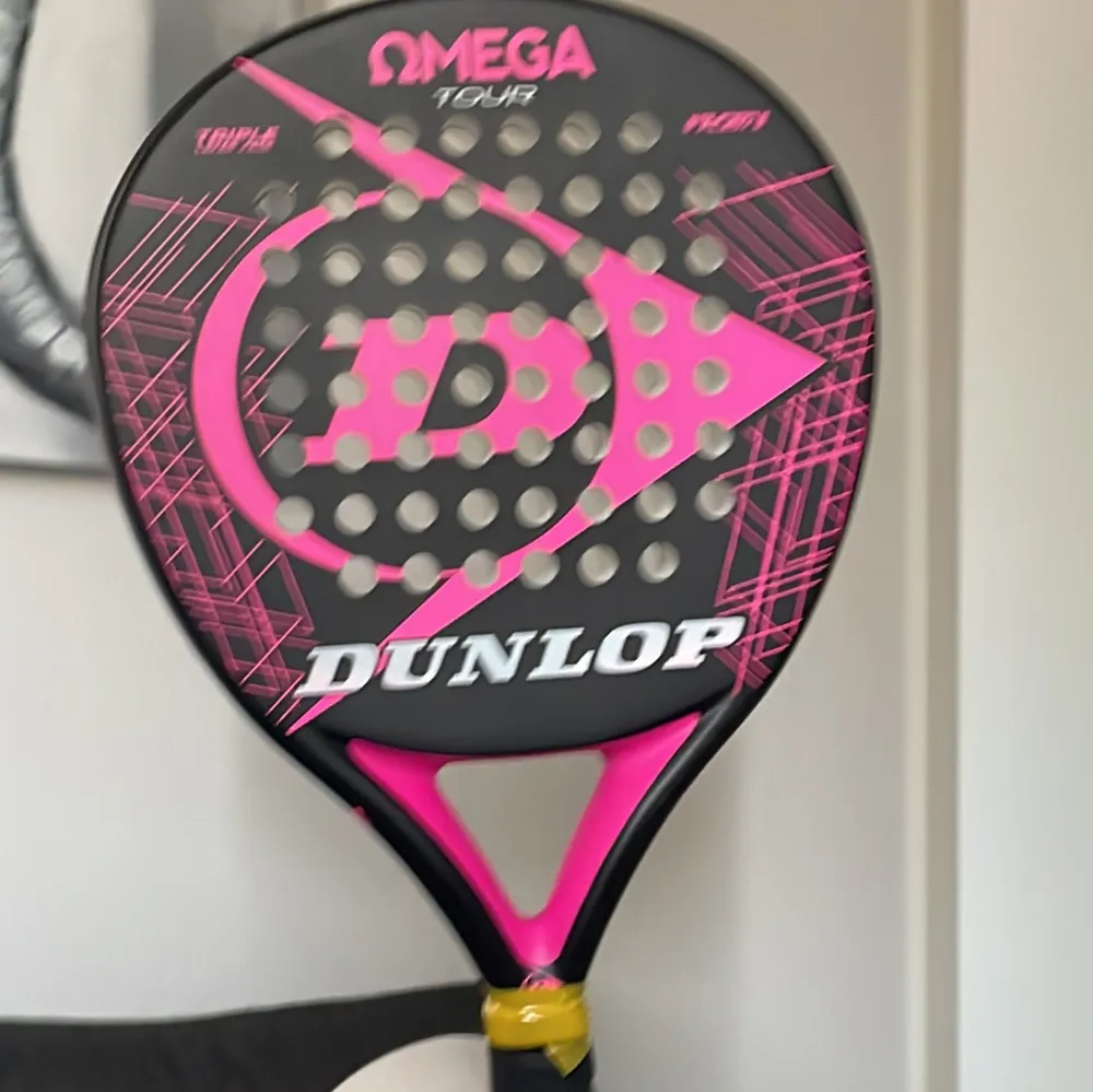 Säljer ett Dunlop Omega Tour padelracket i svart och rosa. Racket har en rund form med ett stort D i mitten och flera små hål för bättre kontroll. Perfekt för både nybörjare och erfarna spelare som vill ha en pålitlig racket på banan. 🎾. Muu.