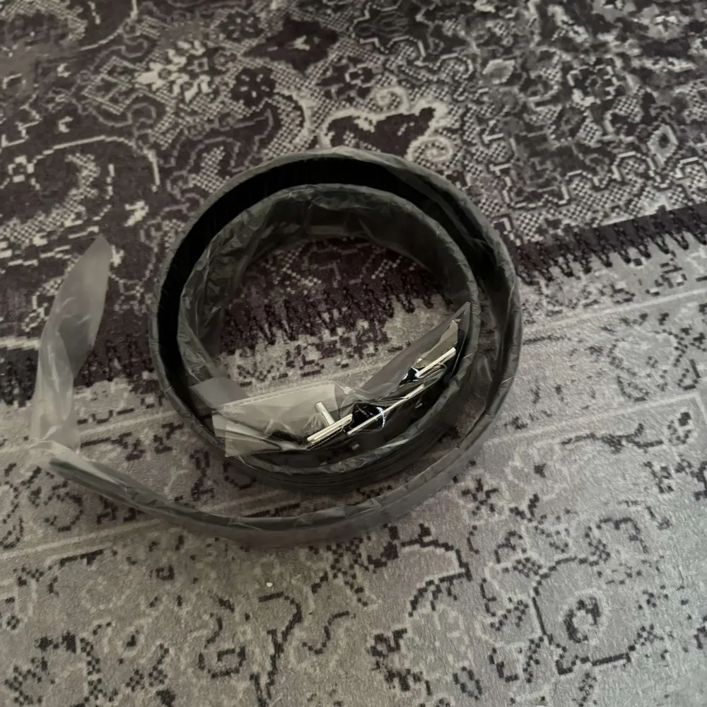 Snyggt svart bälte med ett stort silverfärgat H-format spänne. Perfekt för att ge en stilren touch till din outfit. Bältet är tillverkat i ett elegant material och har en klassisk design.. Muu.