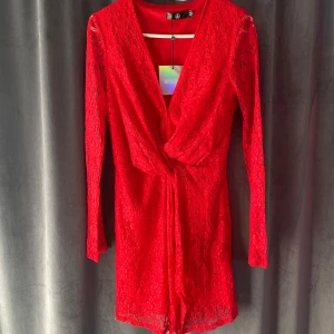 Röd spetsklänning med omlott - Snygg röd spetsklänning från Missguided med omlott-design och långa ärmar. Perfekt för en kväll ute eller en speciell tillställning. Klänningen har en v-ringad fram och är tillverkad i ett vackert spetsmaterial.