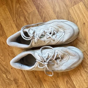 Ozweego beige sneakers Nike - Säljer ett par beiga Nike sneakers med snörning. Skorna har en rund tå och en stilren design med diskreta detaljer. Perfekta för en avslappnad stil.