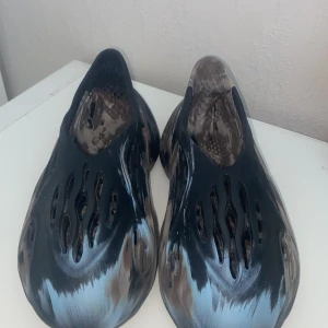  skor i marmorliknande mönster - Unika skor med ett marmorliknande mönster i svart, brun och beige. Skorna har en futuristisk design med flera öppningar för ventilation och komfort. Perfekta för en avslappnad stil.