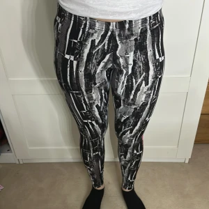 Svartvita leggings med rosa text - Snygga svartvita leggings med abstrakt mönster och rosa texten '#GET STARTED' längs benet. Perfekta för träning eller en avslappnad dag. De har en tight passform och är tillverkade i ett stretchigt material för bästa komfort.