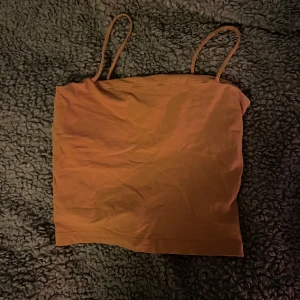 Brun tubtopp med smala axelband - Säljer en enkel och stilren brun tubtopp med smala axelband. Perfekt för varma sommardagar eller som ett basplagg i garderoben.