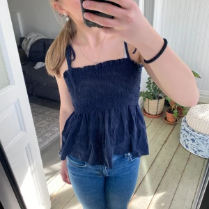 Mörkblå ärmlös topp från Shein - Säljer en söt mörkblå ärmlös topp från Shein med smockdetaljer och knytband på axlarna. Perfekt för varma dagar och kan enkelt matchas med jeans eller kjol. Toppen har en luftig passform och är tillverkad i ett mjukt material.