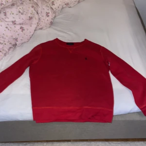 Röd tröja från Polo Ralph Lauren - Säljer en snygg röd tröja från Polo Ralph Lauren med det klassiska logotypbroderiet på bröstet. Tröjan har långa ärmar och en rund halsringning. Perfekt för en stilren look. Den passar för ungdomar cirka 170