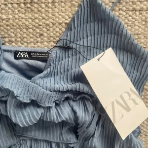 Blå omlottklänning från Zara - Säljer en snygg blå omlottklänning från Zara med volanger och smala axelband. ANVÄND EN GÅNG, ingen prislapp!!!🤍🤍
