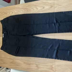 Svarta kostymbyxor från Hunkydory - Eleganta svarta kostymbyxor från Hunkydory med en stilren design. Byxorna har en dragkedja och hyska för stängning. Perfekta för en formell look.