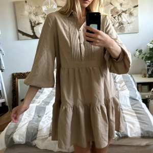 Beige klänning med volangdetaljer - Säljer en stilren beige klänning med volangdetaljer och knappar framtill. 🤎 