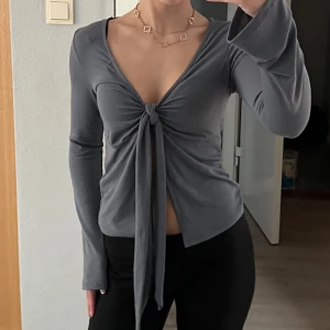 Långärmad knyt topp - Snygg grå/blå långärmad topp från Gina med knyt framtill. Toppen har en v-ringad design och är perfekt för en stilren look. Materialet är mjukt och bekvämt. Lite nopprig på t.ex. armarna men annars fint skick!