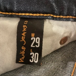 Mörkblå jeans från Nudie Jeans - Snygga mörkblå jeans från Nudie Jeans med klassisk femficksdesign och orange sömmar. Perfekta för en stilren look. Midjan är normalhög och passformen är straight.