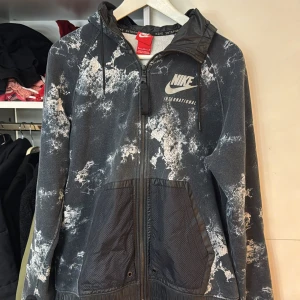 Svart och vit mönstrad jacka från Nike - Säljer en cool svart och vit mönstrad jacka från Nike med dragkedja och huva. Jackan har ett unikt mönster och Nike-logga på bröstet. Perfekt för en sportig look!