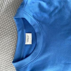 Blå tröja från ONLY - Säljer en superfin blå sweatshirt från ONLY med rund halsringning och långa ärmar. Perfekt för en avslappnad stil. Tröjan har ribbade muddar vid ärmslut och nederkant. Knappt använd.