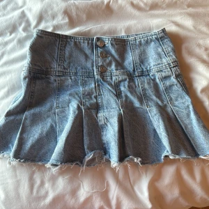 Jeanskjol med knappar - Säljer en cool jeanskjol med knappar framtill och rå kant. Kjolen har en lätt utställd form och är perfekt för en avslappnad stil. Passar bra till en enkel t-shirt eller en snygg blus.