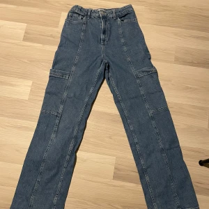 Blå cargopants med fickor - Säljer ett par blå cargopants med flera praktiska fickor. Byxorna har en normal passform och är perfekta för en avslappnad stil. De har en dragkedja framtill och är tillverkade i ett slitstarkt material. Väldigt stretchiga! 