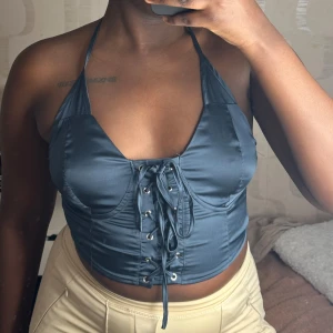 Mörkblå korsett/halterneck topp med snörning - Snygg mörkblå korsett-topp med snörning framtill och dragkedja bak. Toppen har en halterneck-design och är perfekt för en kväll ute. Materialet har en glansig finish som ger en lyxig känsla 💙