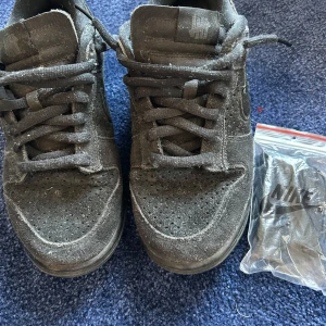 Svarta Nike SB Dunk x undefeated  - Säljer ett par svarta Nike Dunk sneakers. Skorna har en klassisk design med snörning och en robust sula. Perfekta för vardagsbruk och stilrena nog att matcha med det mesta. Levereras i originalkartong.