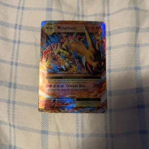 Mega Charizard Pokémonkort - Säljer ett Mega Charizard Pokémonkort med en imponerande design och starka färger. Kortet har en holografisk yta som ger det en extra glans. Perfekt för samlare eller Pokémon-fans som vill utöka sin kortsamling.