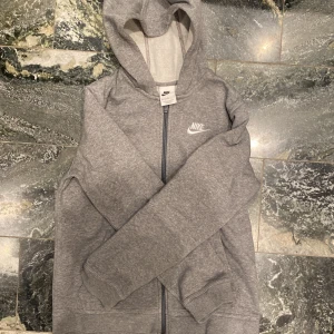Grå hoodie från Nike - Säljer en klassisk grå hoodie från Nike med dragkedja och huva. Perfekt för en avslappnad stil. Storlek 147-158 cm 