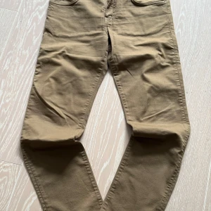 Beige byxor från J.Lindeberg strl: 30/32 - Snygga beige byxor från J.Lindeberg i storlek M. Byxorna har en klassisk design med normal passform och är tillverkade i ett bekvämt bomullsmaterial. Perfekta för en stilren look.