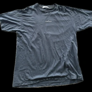 Blå t-shirt från Stone Island - Säljer en blå t-shirt från Stone Island med tryck på både fram- och baksidan. T-shirten har en klassisk rund hals och korta ärmar. Perfekt för en avslappnad stil.