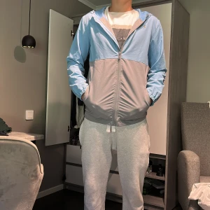 Blå och grå vindjacka från under armour - Säljer en stilren vindjacka i ljusblått och grått med huva och dragkedja framtill. Perfekt för dig som gillar en clean och sportig look. Pris kan diskuteras 