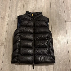 Svart dunväst från Parajumpers - Snygg svart dunväst från Parajumpers med hög krage och två dragkedjeförsedda fickor framtill. Västen har quiltad design och coolt PJS-märke på ryggen. Perfekt att slänga över en hoodie för extra värme. Materialet är glansigt och känns riktigt lyxigt. Det är bara att skriva till mig om frågor eller flera bilder:)