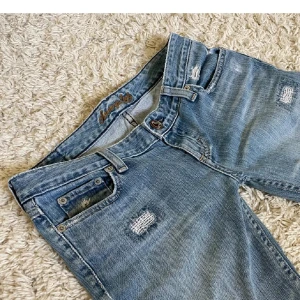 Bootcut jeans i ljusblå denim - Snygga bootcut jeans från American Eagle i ljusblå denim med slitna detaljer och lagade partier. Låg midja. 73 cm : innerben och 36,5: midjemått ☺️
