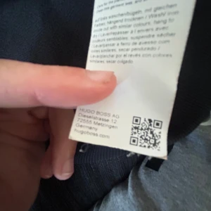 Svart sweatshirt från Hugo Boss - Svart sweatshirt från Hugo Boss med klassisk rund hals och ribbade muddar. Tröjan har en stilren design med röd etikett i nacken där det står HUGO. Materialet är mjuk bomull som känns skön mot huden. Perfekt för dig som gillar enkel och snygg streetstil.