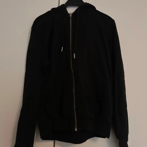 Svart hoodie med dragkedja och huva - Svart hoodie med hel dragkedja framtill och huva med snörning. 